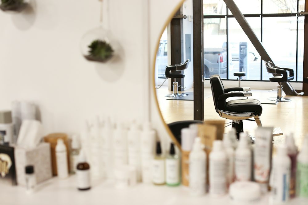 Salon chairs reflected in a round mirror above a counter of hair products